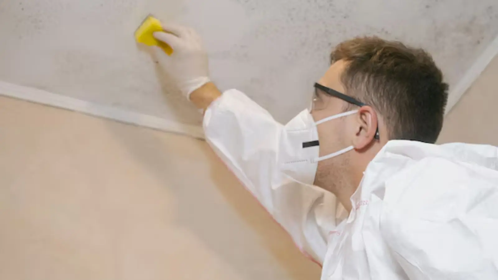 Person in a mask and protective suit wiping mold from a wall